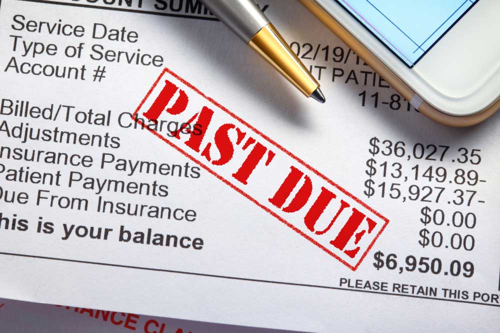 Medical bill stamped "PAST DUE" shows a large unpaid balance, pen and smartphone resting on the statement.