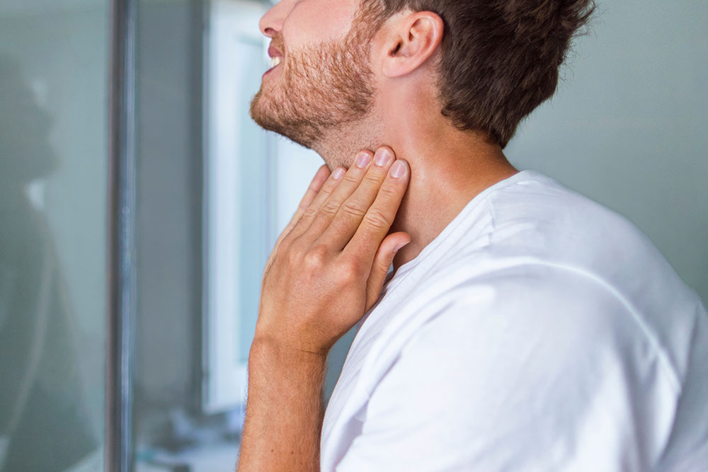 Man checking his throat for thyroid nodules or discomfort, a potential early sign of thyroid cancer.