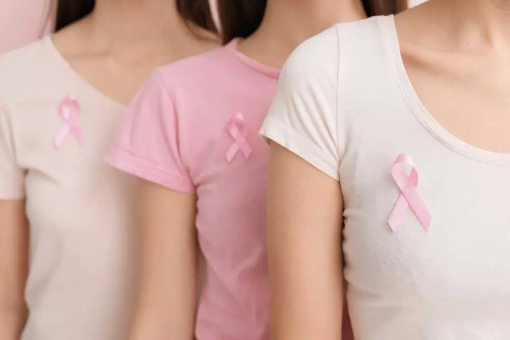 Three women in pink and white shirts stand in a row, each with a pink ribbon pinned to their chest, symbolizing breast cancer awareness and raising support for those experiencing thyroid cancer symptoms. | Cancer Biopsy & FNA Doctor in Los Angeles - Dr. Celina Nadelman