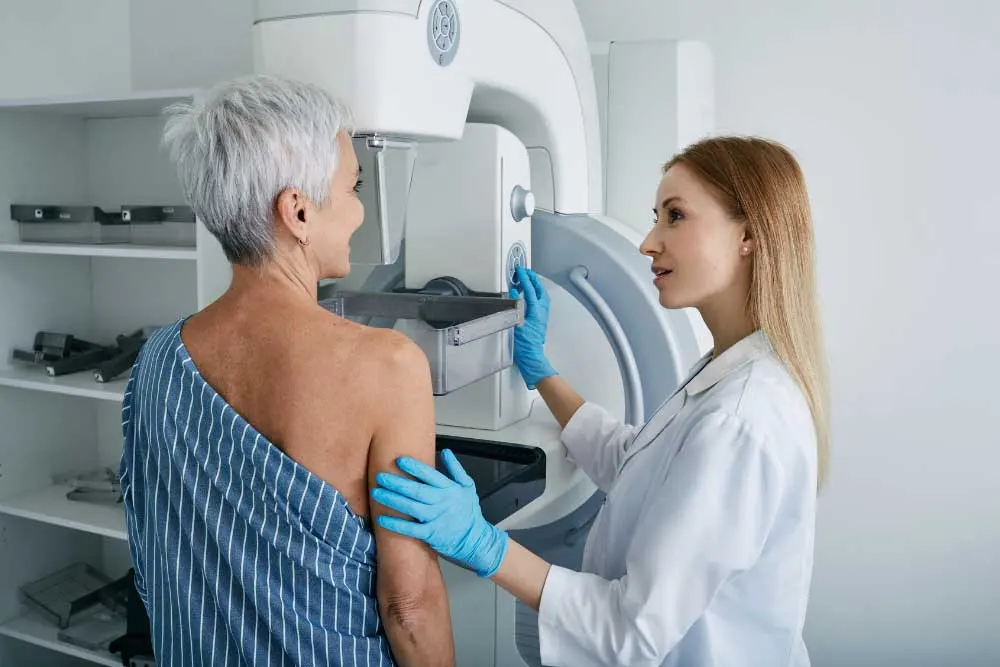 A healthcare professional prepares a patient for a mammogram using a medical imaging machine in a clinical setting, similar to procedures for thyroid cancer diagnosis in Southern California. | Cancer Biopsy & FNA Doctor in Los Angeles - Dr. Celina Nadelman